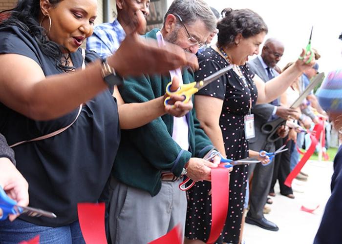 A group of people face one direction with scissors in their hands and pieces of red ribbon